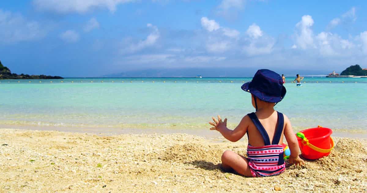 沖縄のビーチでバケツを持って砂遊びをする赤ちゃんの後ろ姿