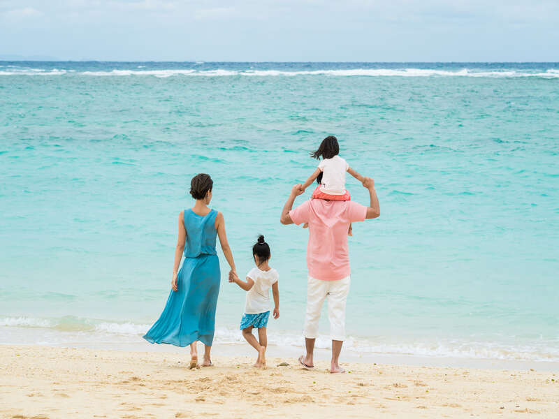 沖縄のエメラルドグリーンの海辺を歩く子連れファミリー