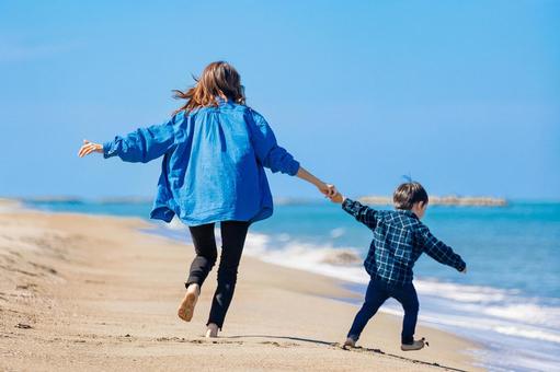 沖縄の砂浜でママと子どもが手をつないで走る後ろ姿