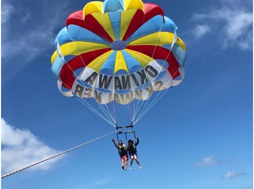 沖縄の青い空と海をバックにパラセーリングを楽しむ様子